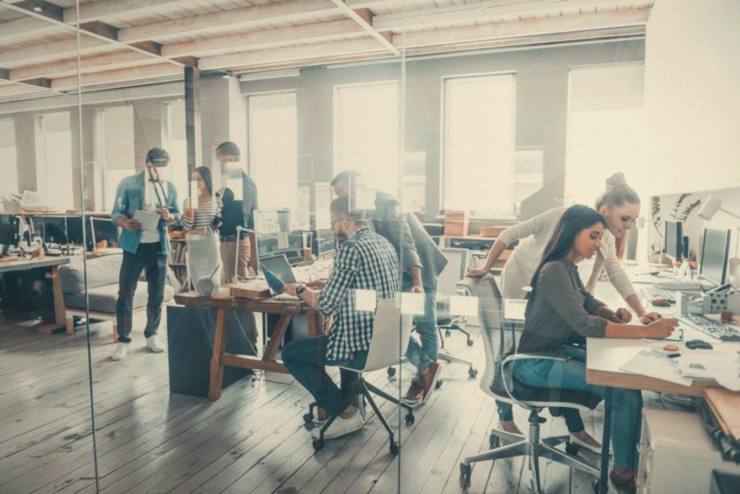 Des professionnels collaborent dans un bureau lumineux à aire ouverte, vu à travers une paroi vitrée