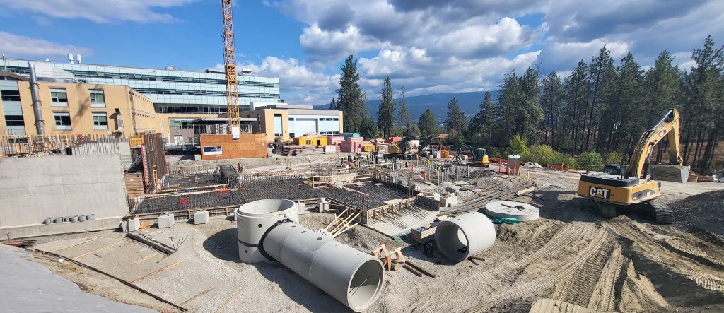 Un chantier d’installation d’Earth Tube Systems, avec de grandes sections de tubes souterrains en béton, une excavatrice et des fondations en cours